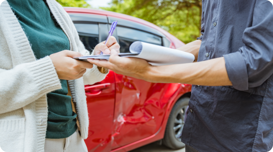 Une voiture endommagée avec deux personnes au premier plan signant des papiers.