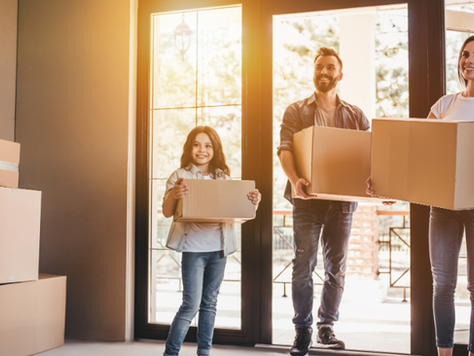 Les parents et l’enfant portent un carton de déménagement dans une maison.