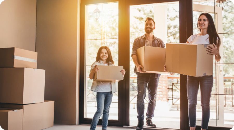 Les parents et l’enfant portent un carton de déménagement dans une maison.