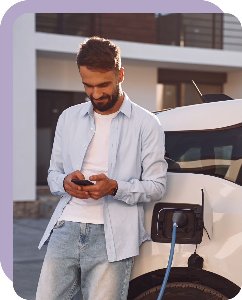 Un giovane è al cellulare e si appoggia a un’auto elettrica in ricarica.